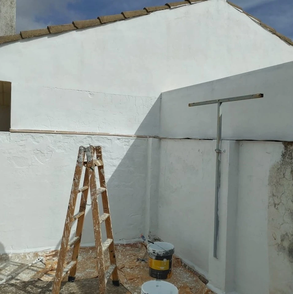 Trabajos de pintura en fachada blanca con escalera de madera y botes en Aguilar de la Frontera