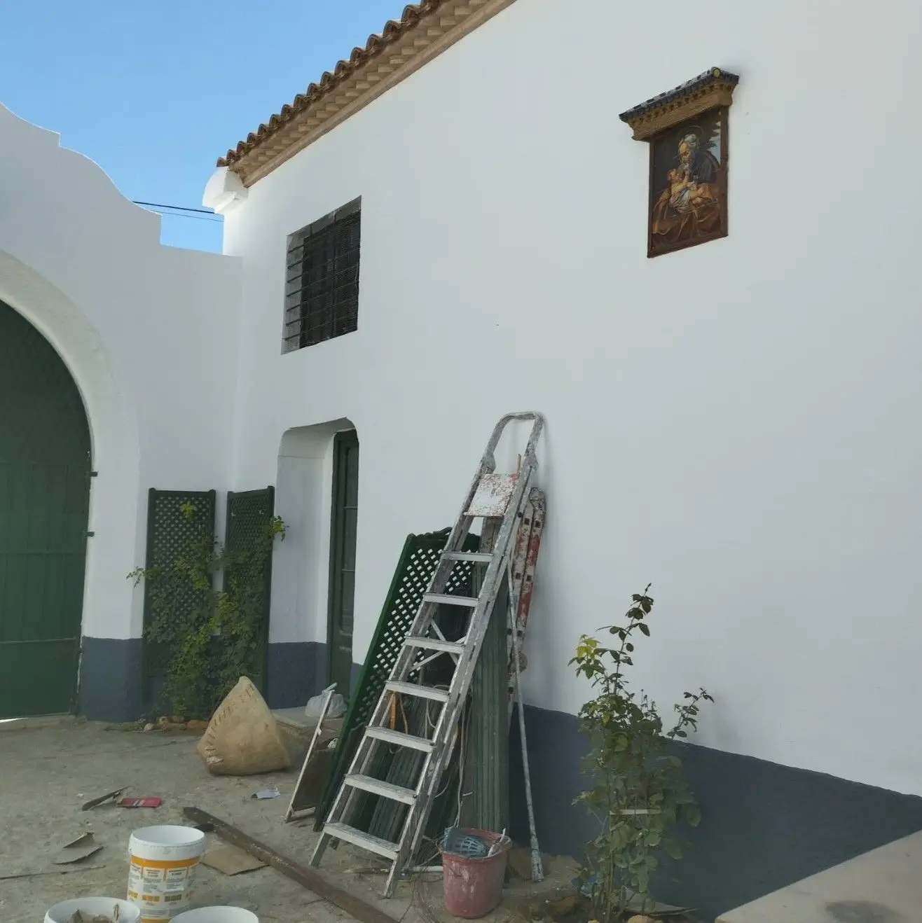 Trabajos de pintura en fachada blanca con zócalo gris y escalera de mano en Aguilar de la Frontera