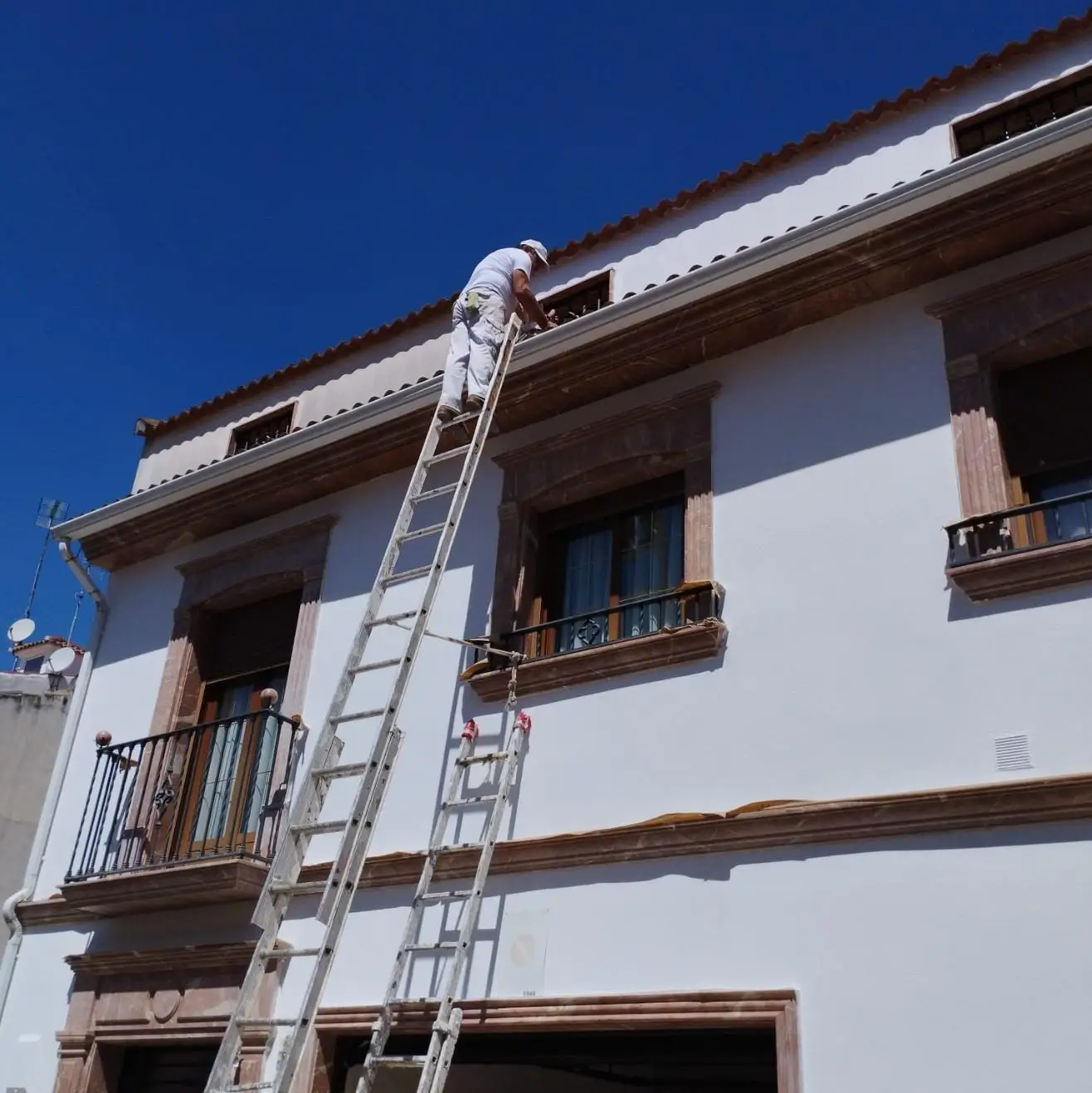 Operario realizando trabajos de pintura en fachada blanca con molduras de piedra en Aguilar de la Frontera