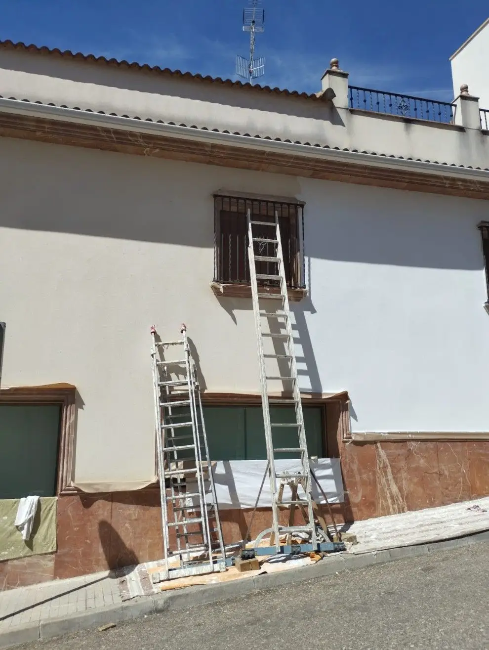 Trabajos de pintura en fachada con escaleras de aluminio y protección de ventanas en Aguilar de la Frontera