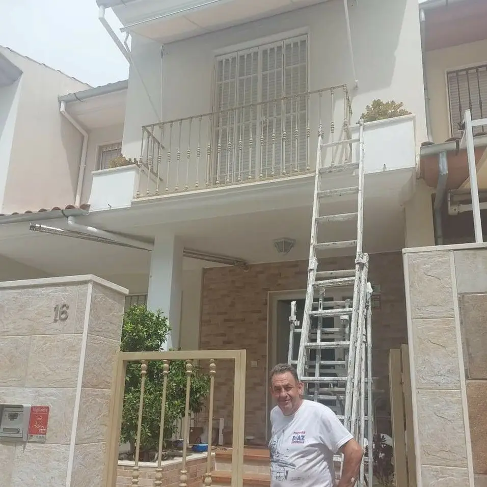 Trabajos de pintura en fachada de vivienda blanca con operario y escalera en Aguilar de la Frontera